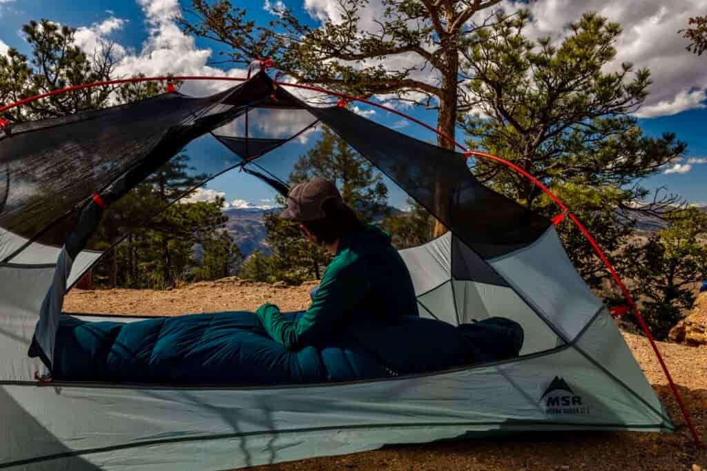 A hiker sits in a tent without the fly overlooking some mountains