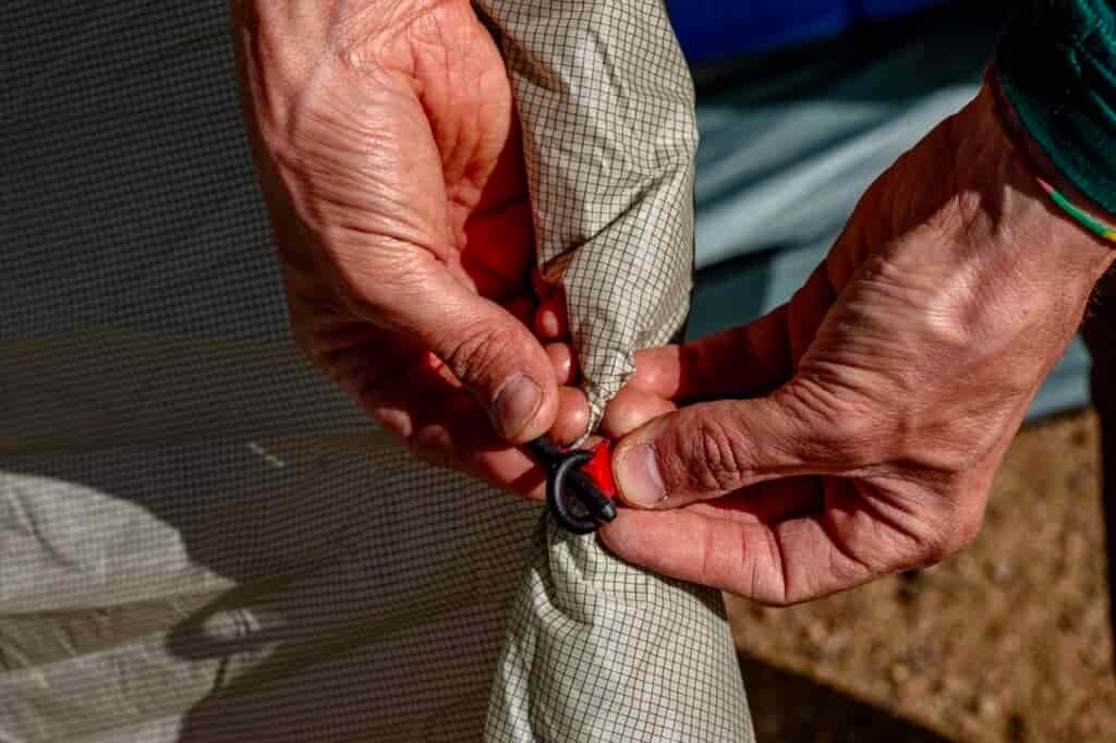 A close up of two hands latching a loop and toggle tie back on a tent door.