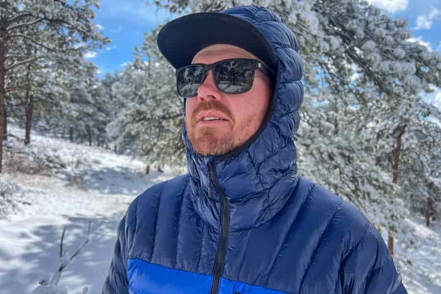 a man standing in a snowy forest. He's wearing a blue jacket looking off into the distance.