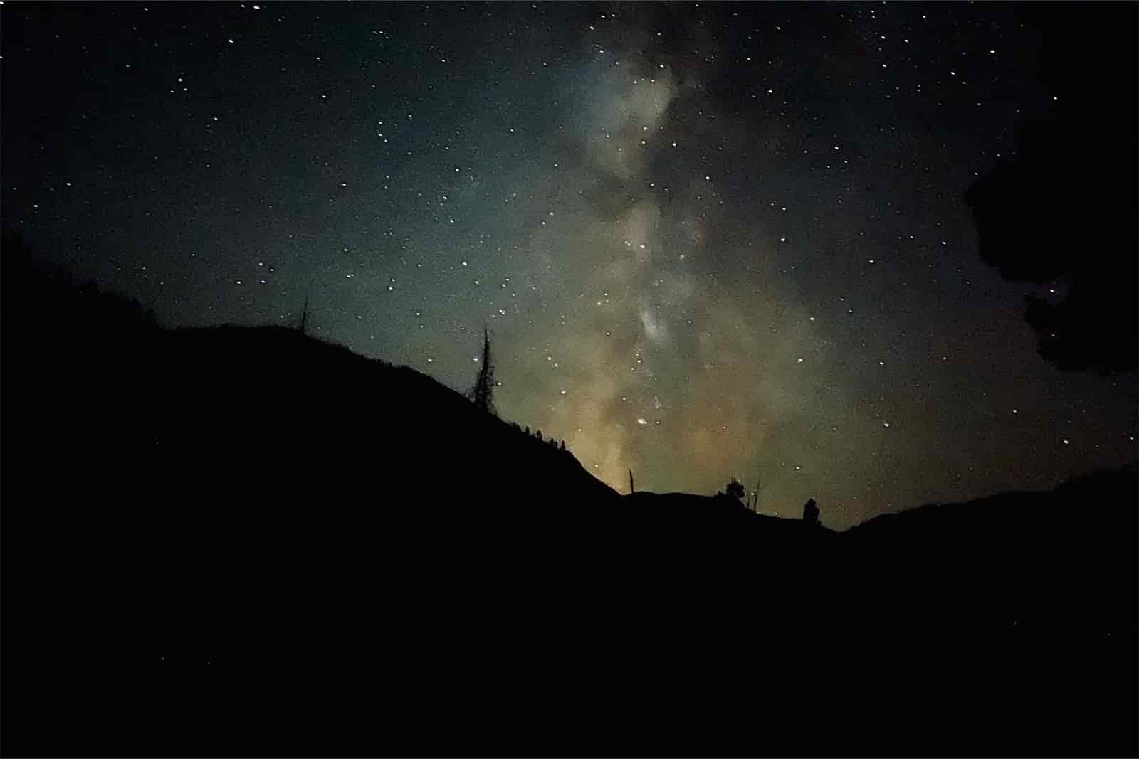 The milky way and stars are visible above a mountain at night.