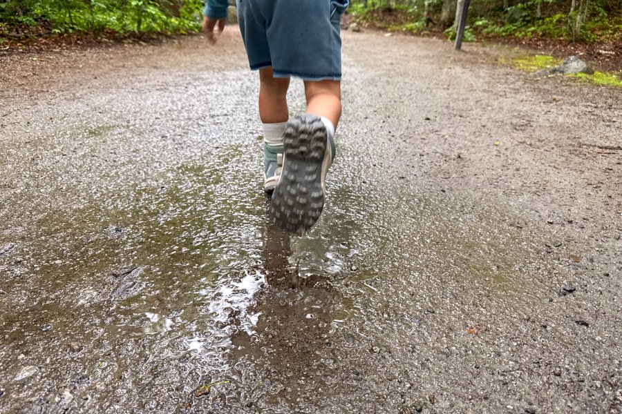 Close-up of child running through a puddle on a forest trail wearing Adidas Terrex AX4R Mid shoes.
