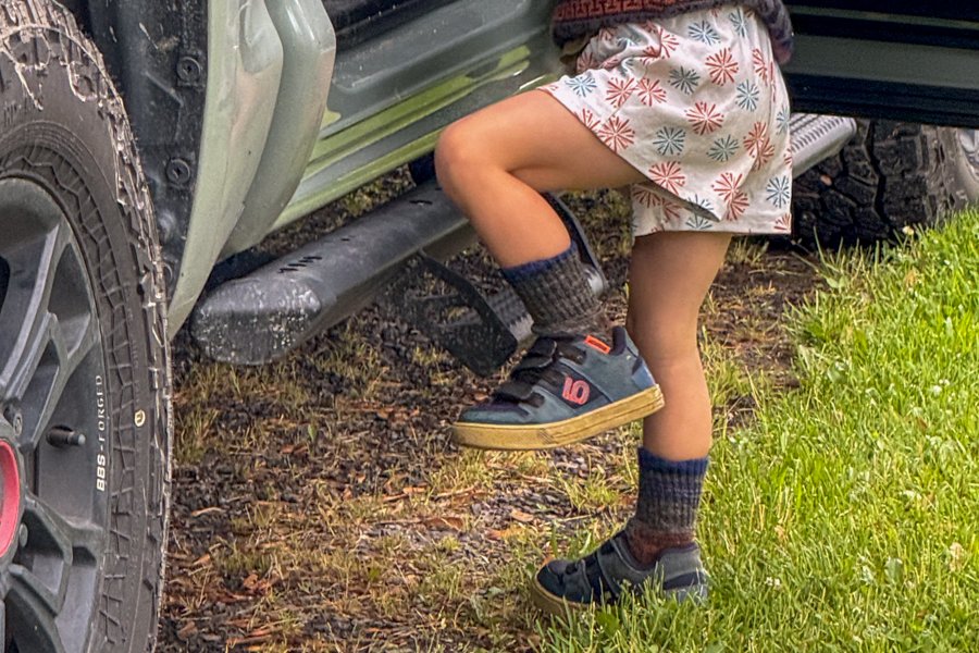 Child wearing Five Ten Freerider shoes stepping into a truck with muddy tires.