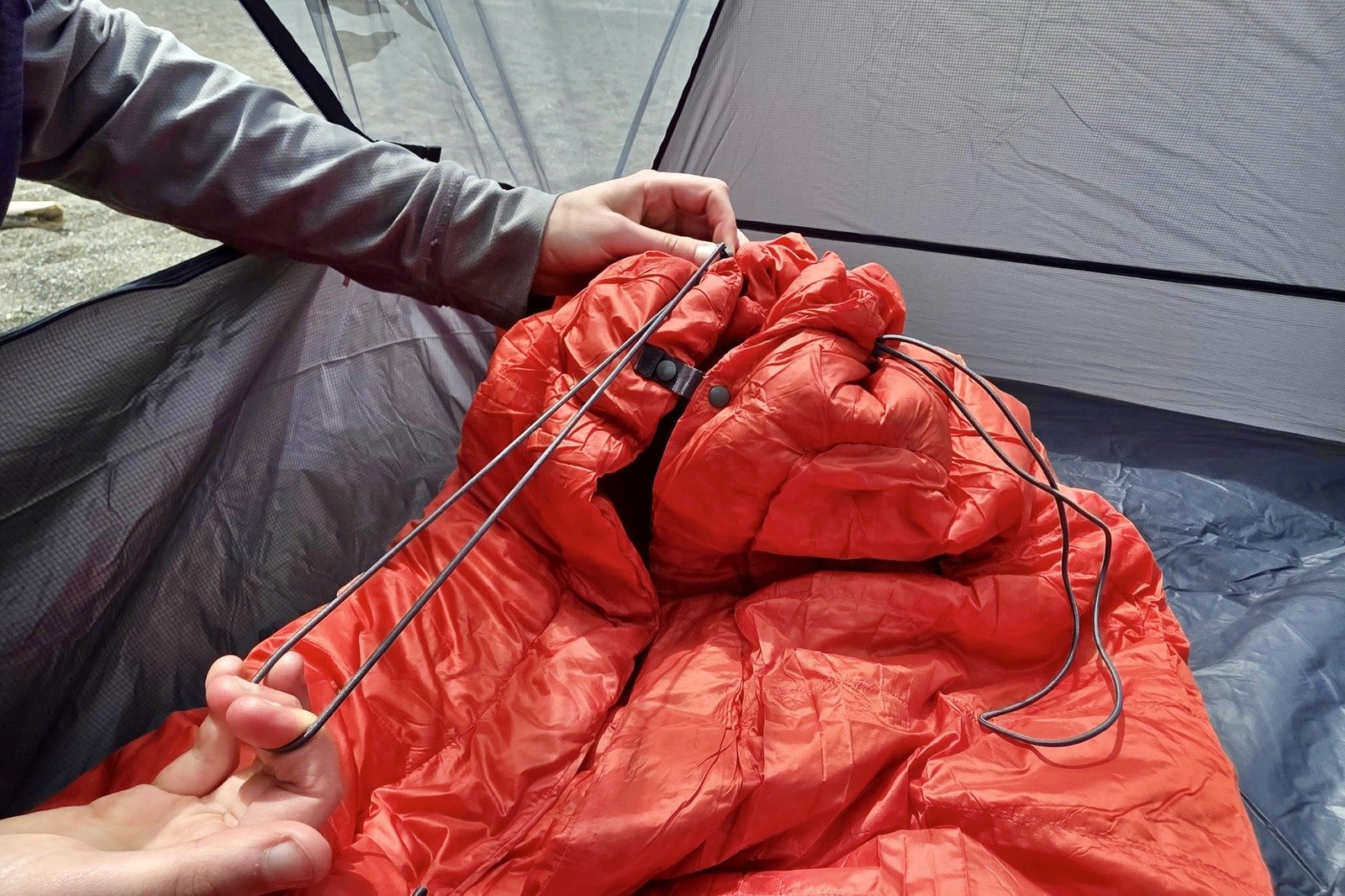 A woman cinches down the foot box of her minimalist sleeping bag.