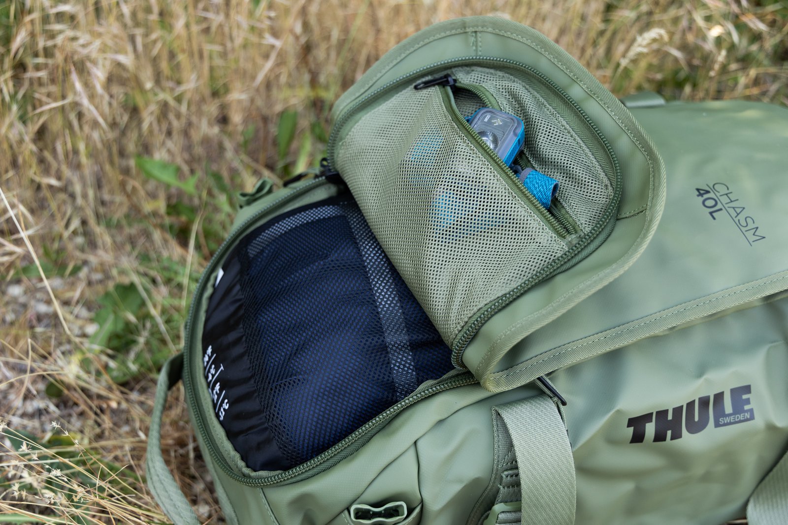 The unique U-shaped lid on one end of the Thule Chasm duffel shown open. Yo can see that it provides easy access to a small accessory pocket inside the lid that is flipped open when the rest of the lid is zipped shut.