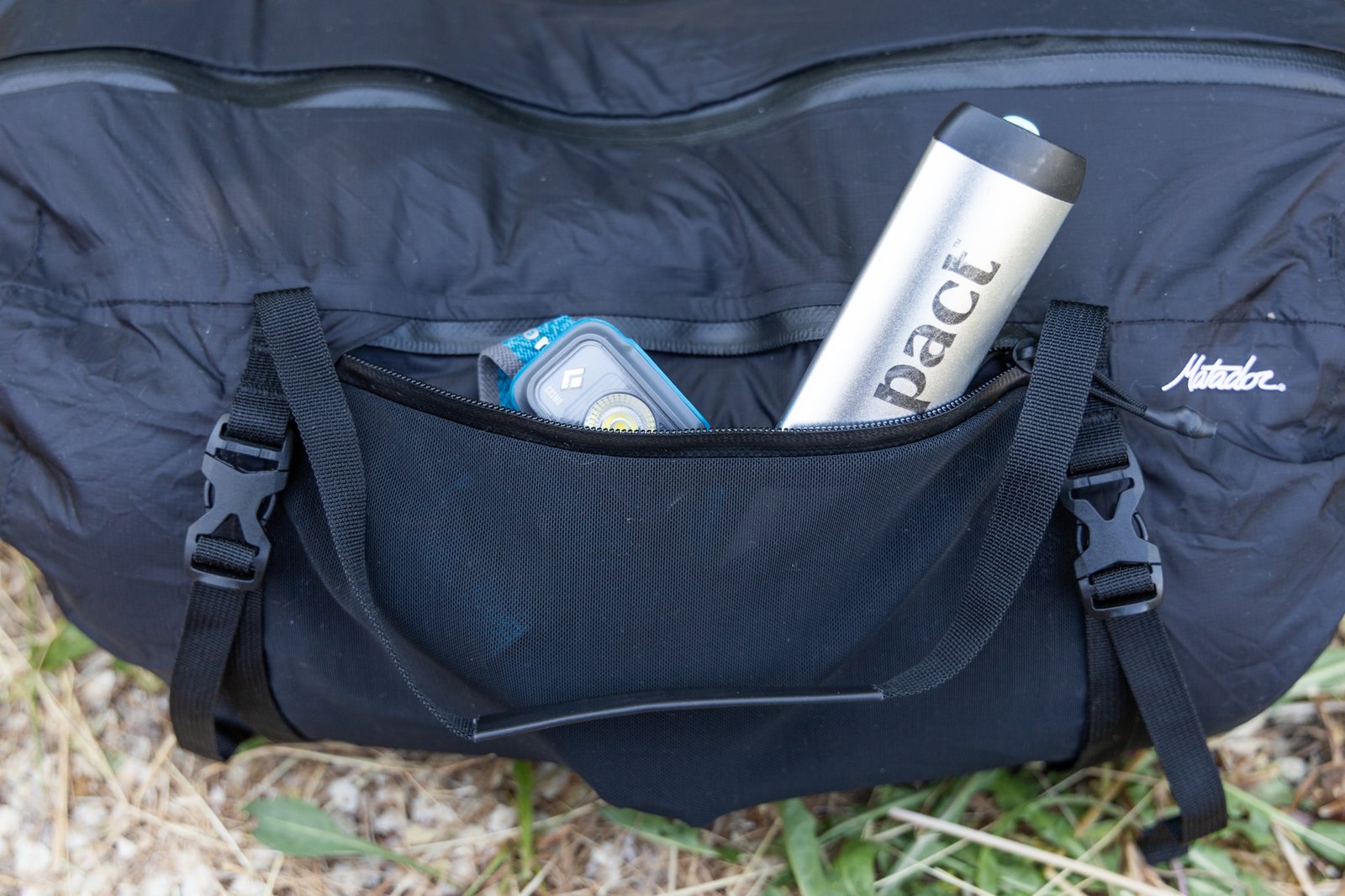 A spade and a headlamp peak out of the open stretch mesh zipper pocket on one side of the Matador Freefly Packable Duffel.