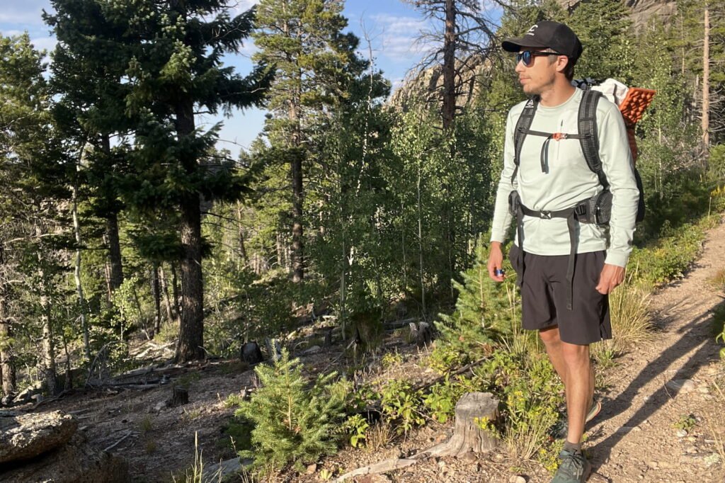 a hiker walks along a wooded trail wearing a light blue base layer and a backpack
