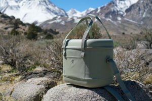 The Hydro Flask Carry Out 20L cooler sits on a rock with mountains in the background.