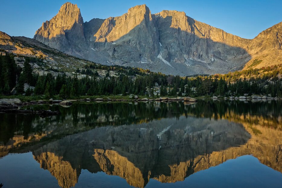 alpenglow on a granite craggy ridgeline reflecting over a lake 