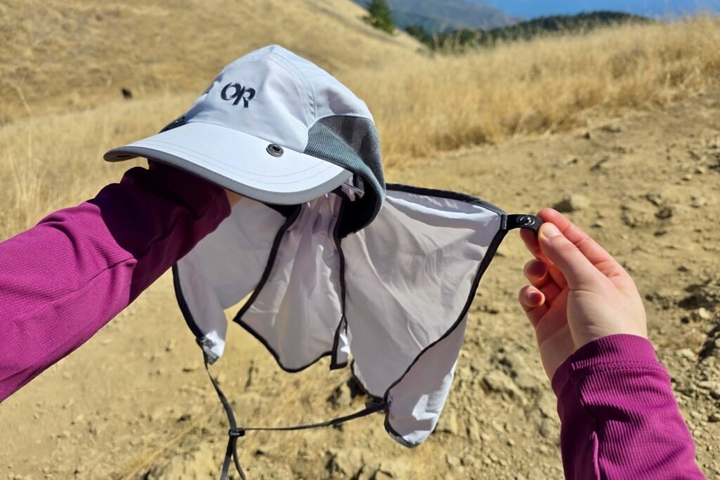 A woman detaches the cape attachment from her sun cap.