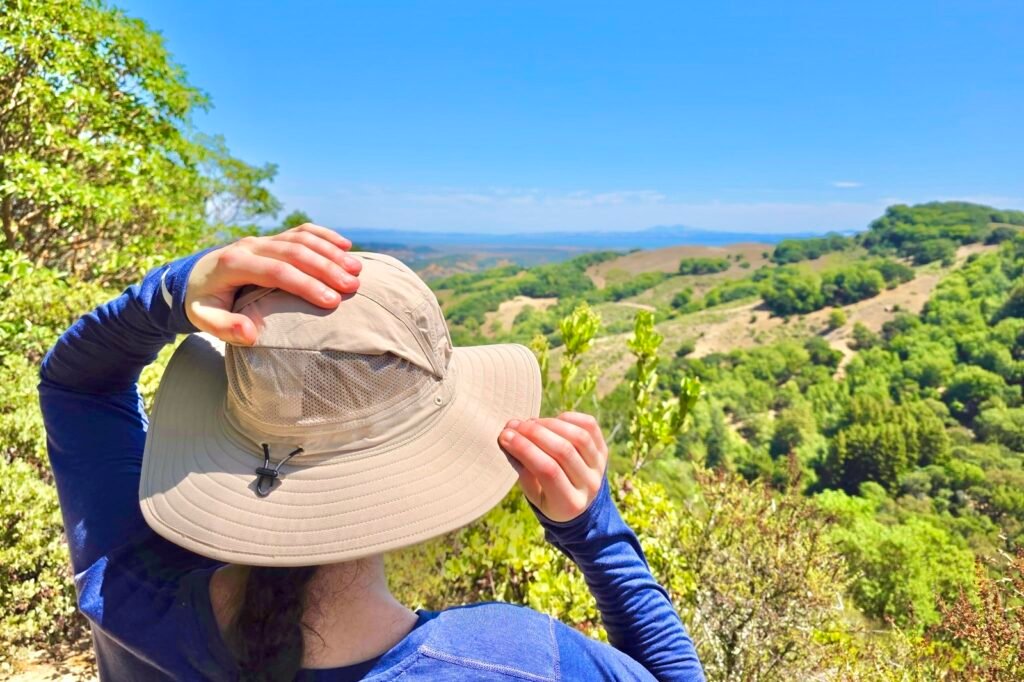 A woman pulls up the mesh panels on her sun hats while stopping at an overlook on the trail.