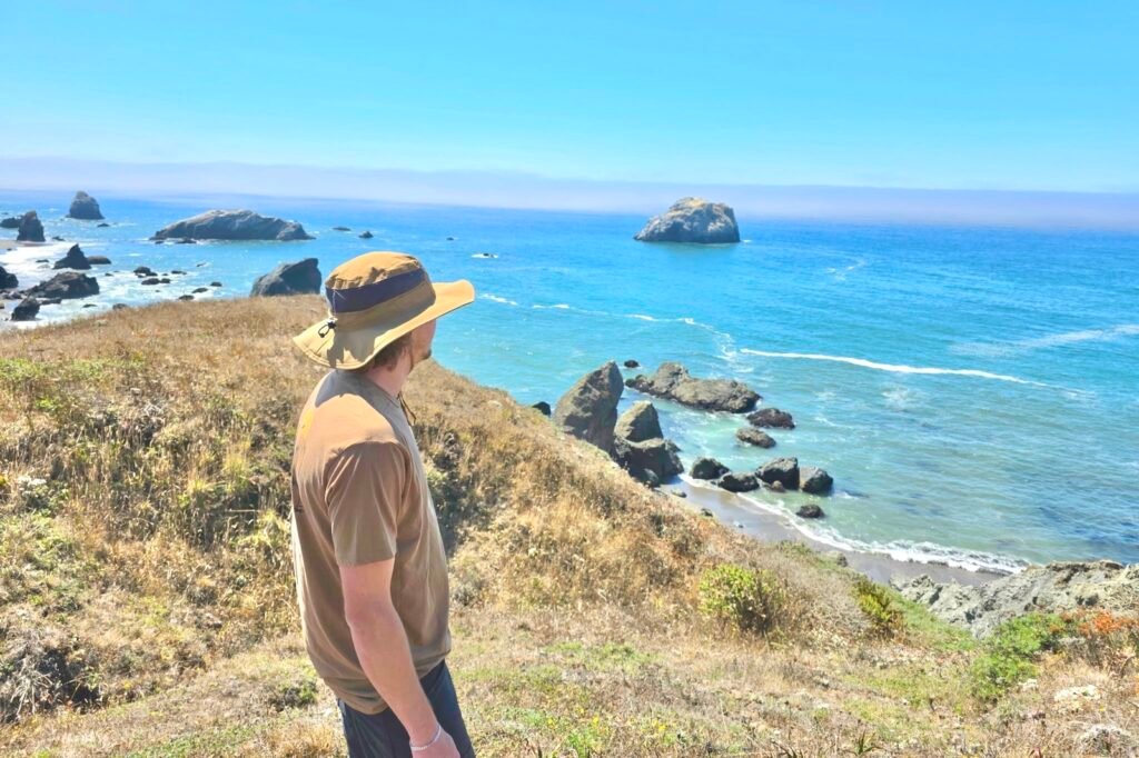 A man stands on a hill overlooking the Pacific Ocean.