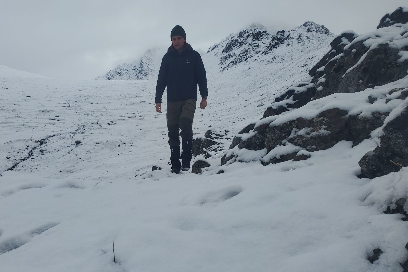 A man hikes in the snowy alpine wearing a rain jacket.