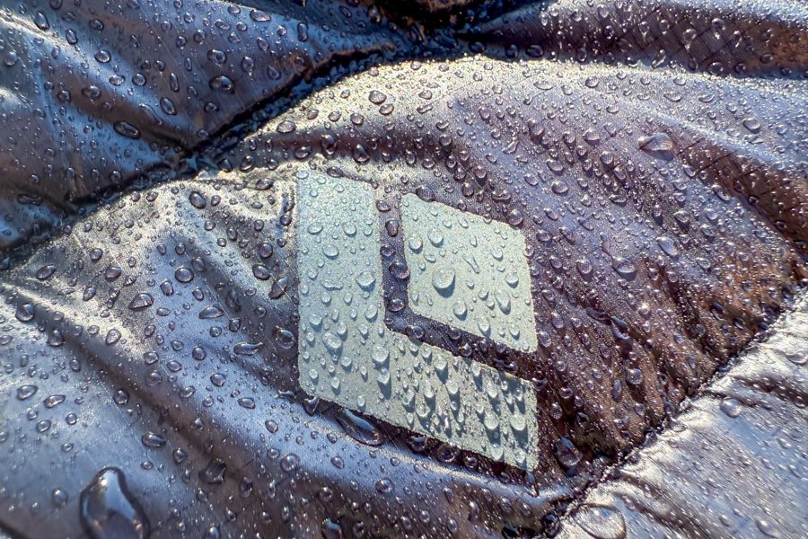 Close-up of the Black Diamond logo on the Deploy Down 0.5 Full Zip Hoody, covered in water droplets demonstrating the jacket’s DWR (durable water repellent) coating.