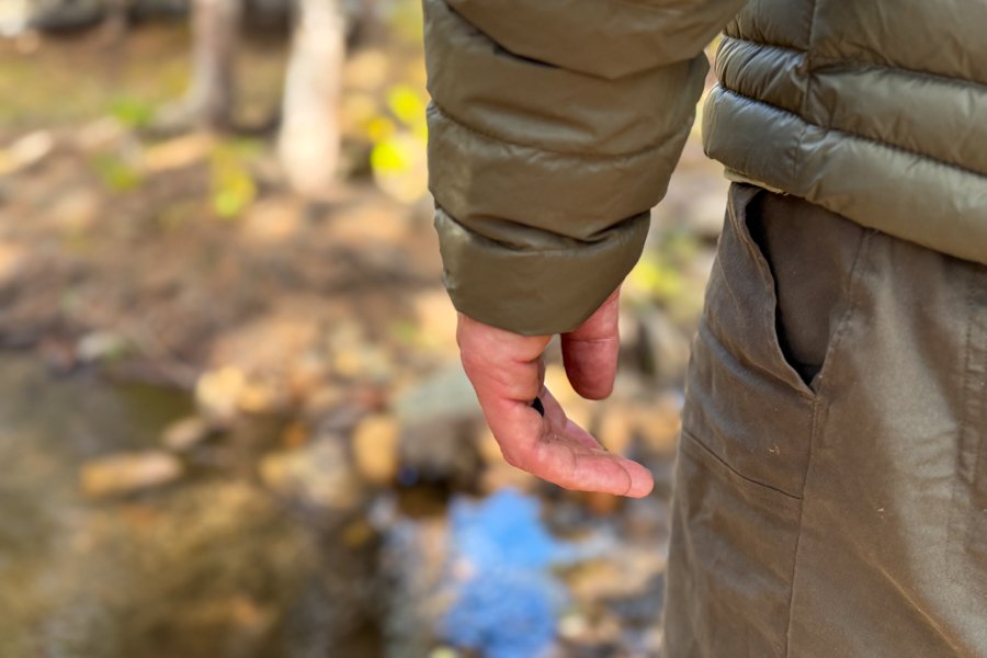Close-up of a person’s hand and sleeve wearing the Decathlon Simond MT100 Down Jacket, showing the snug fit and lightweight baffle design near a creek.