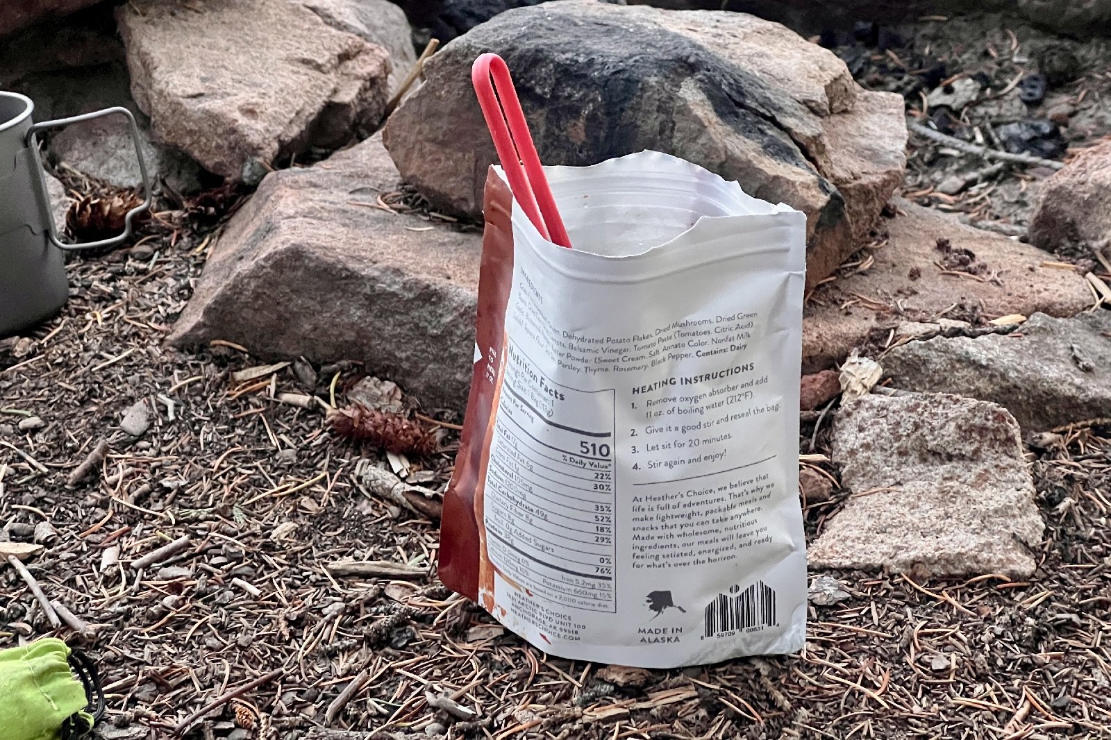 a backpacking meal sits on the ground with a red spork handle sticking out of it