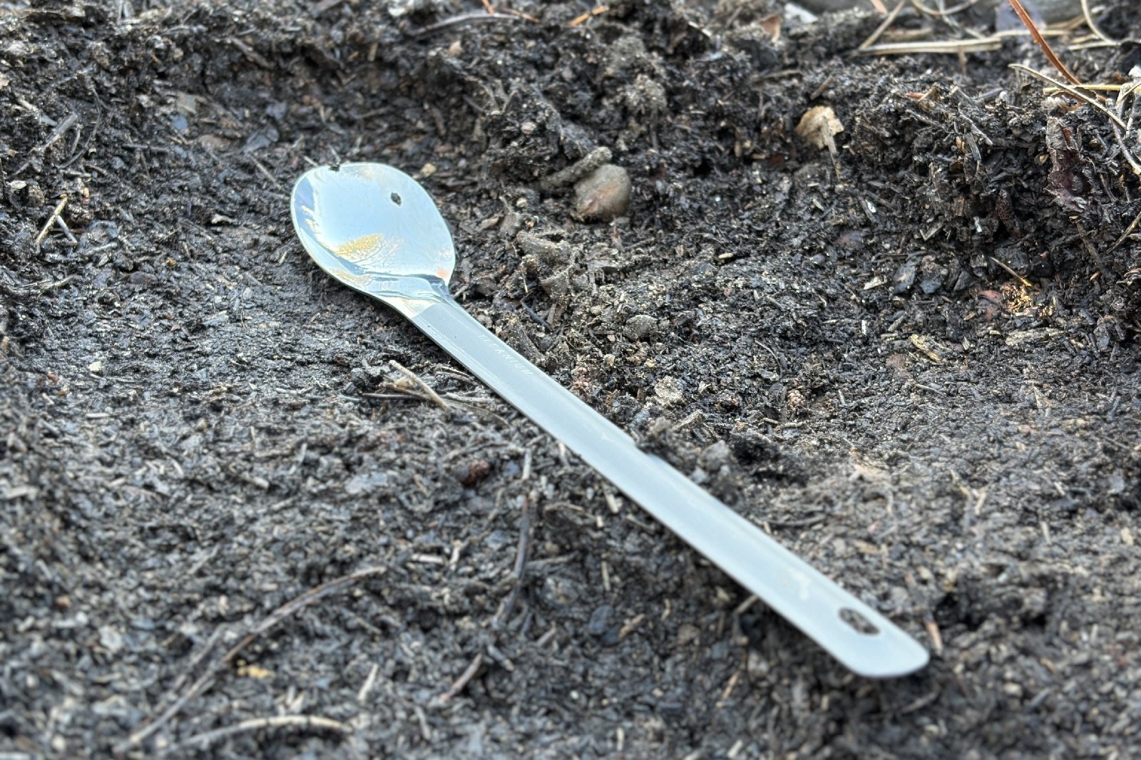 a titanium spoon with a polished bowl lays in the dirt