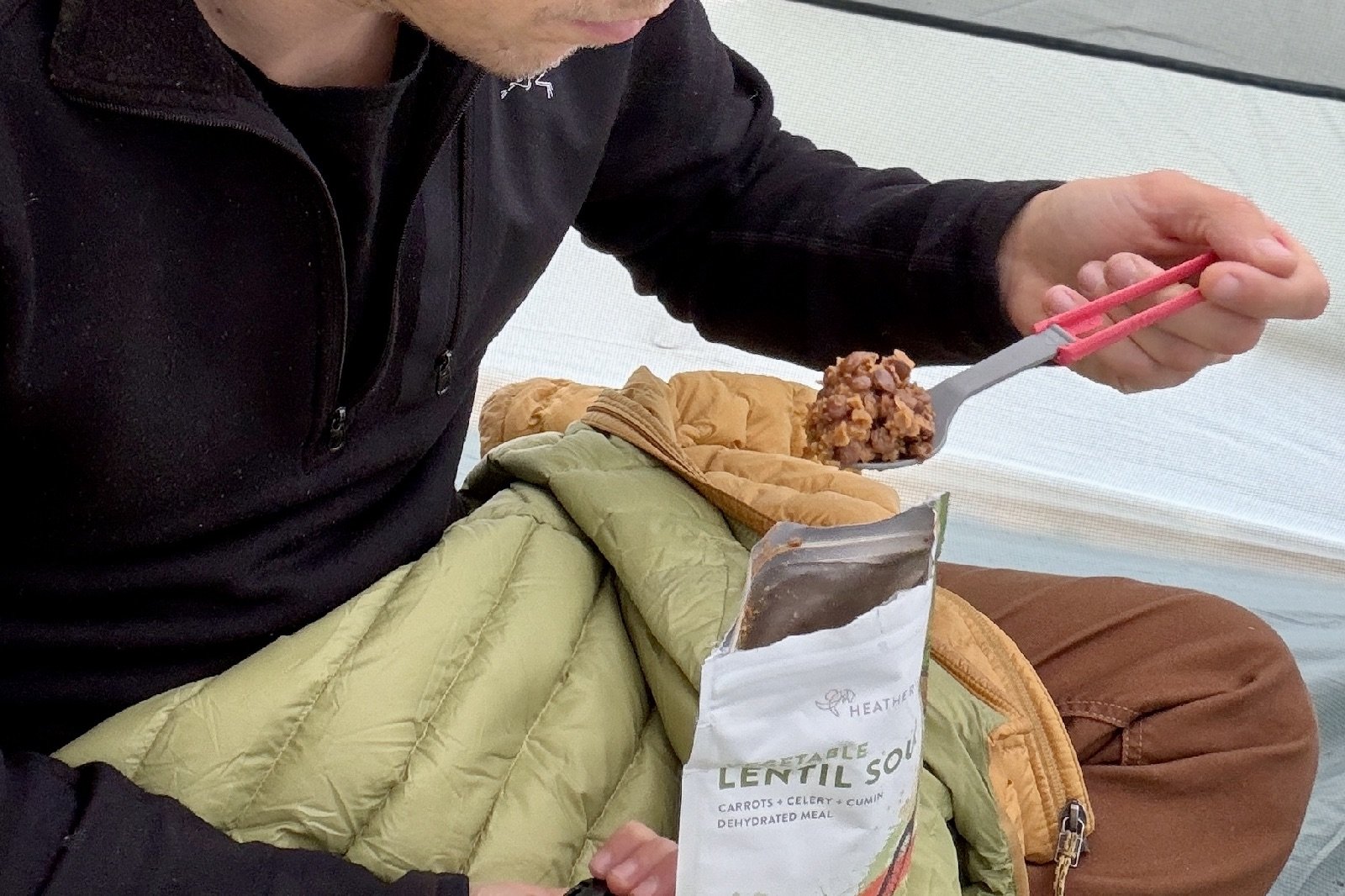 a hiker scoops a bit of food from a backpacking meal with a plastic spork