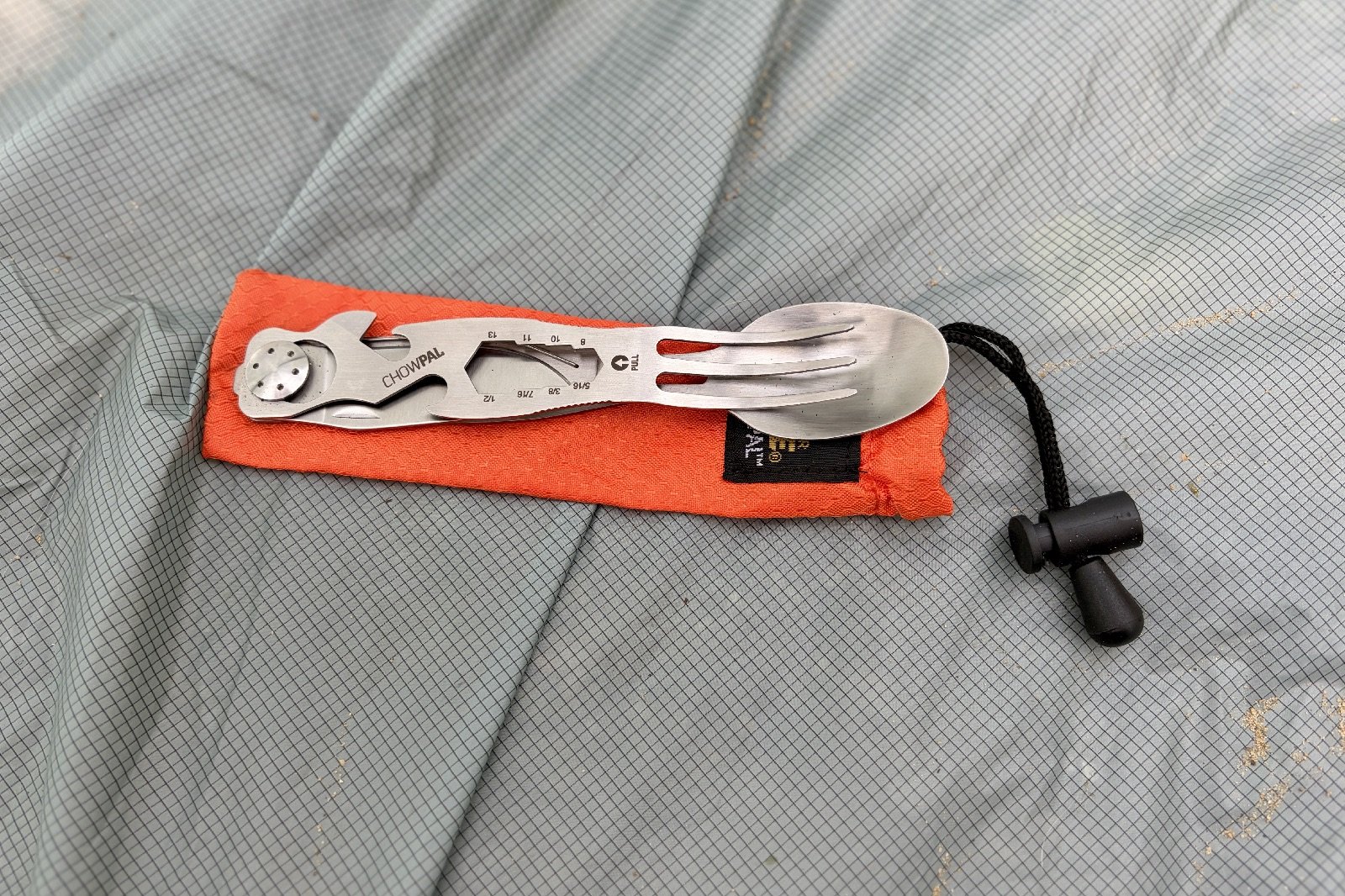 a multi-tool utensil sits folded up on an orange drawstring bag