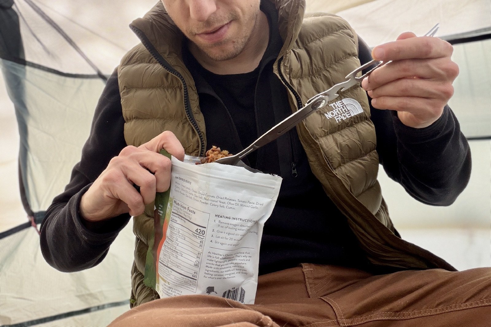 a hiker uses an extended multi-tool utensil to scoop a bite of food out of a meal pouch
