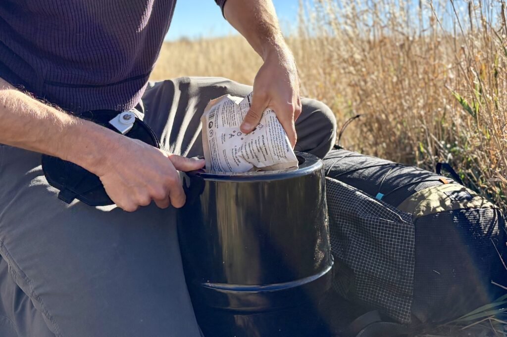 A hiker kneels and packs a food pouch into a black bear canister