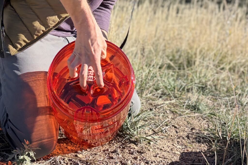 a hiker puts his fingers into the lid dimples of an orange bear canister to twist off the lid