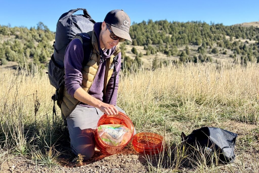 a hiker tips an orange bear canister over to show its inside