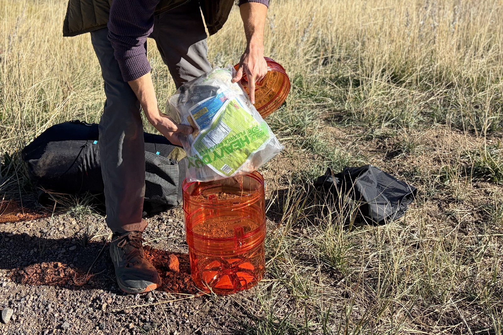 a hiker packs a clear food bag into an orange bear canister