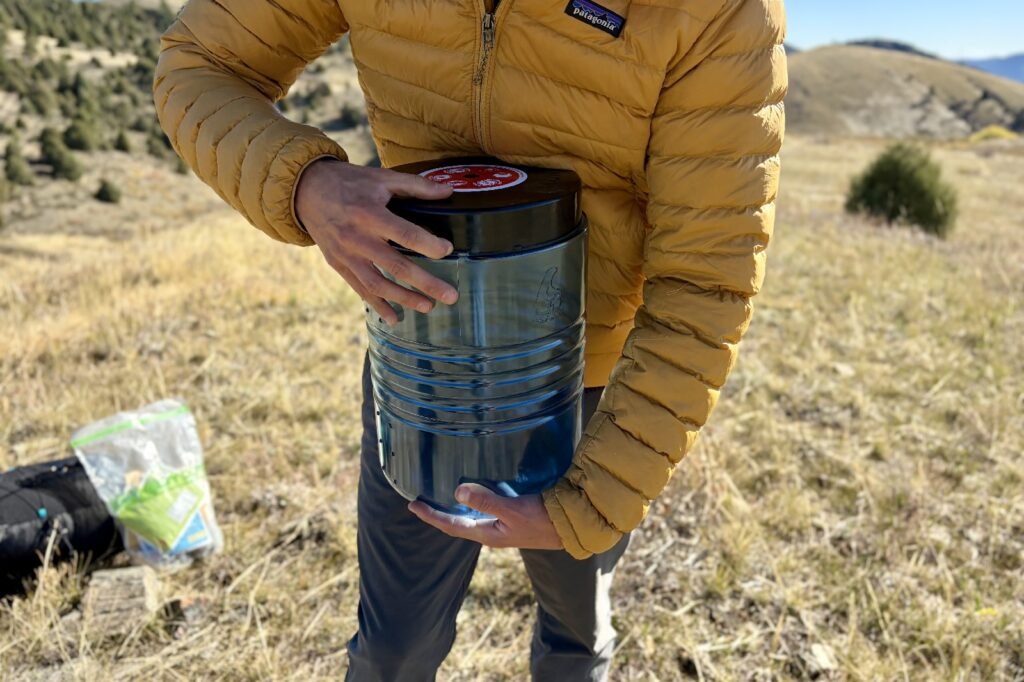 a hiker holds a blue bear canister with one hand and presses the locking mechanism with the other