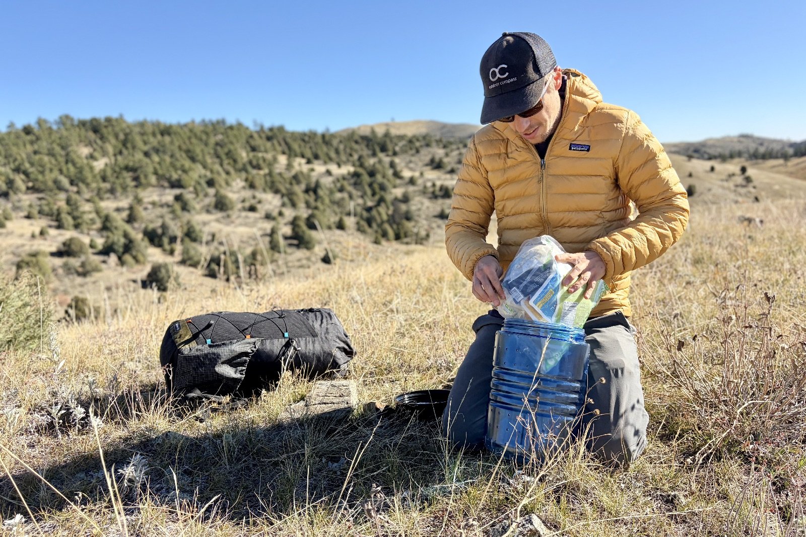 a hiker stuffs a clear food bag into a blue bear canister