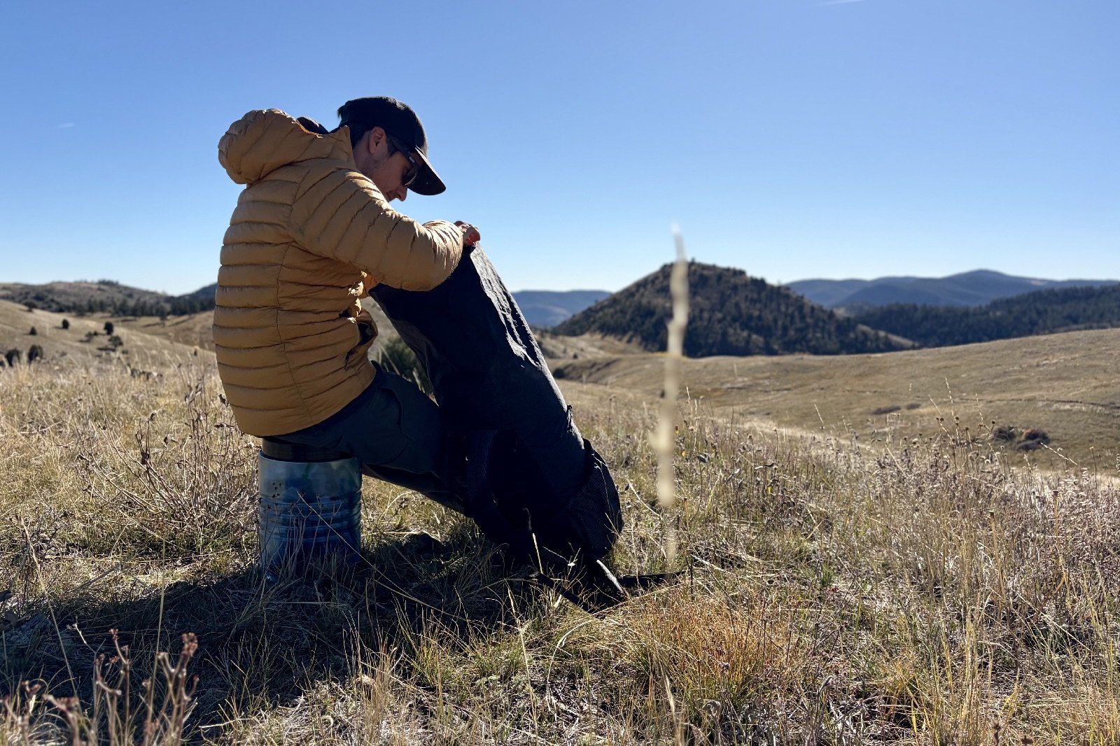 a hiker sits on a blue bear canister as he looks into his backpack