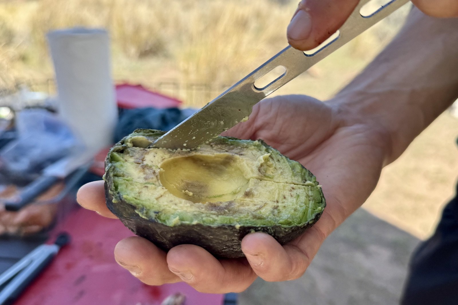 a close up of a pair of hands cutting into an avocado with a knife