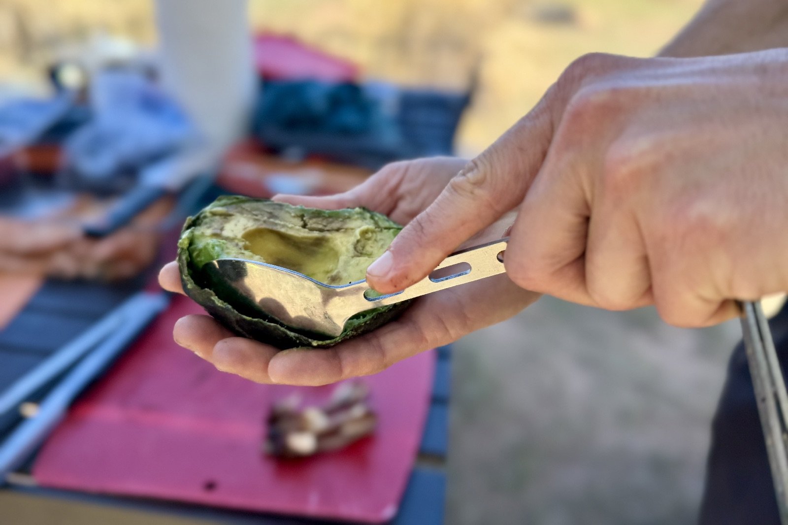 a close up of a pair of hands scooping avocado with a spoon