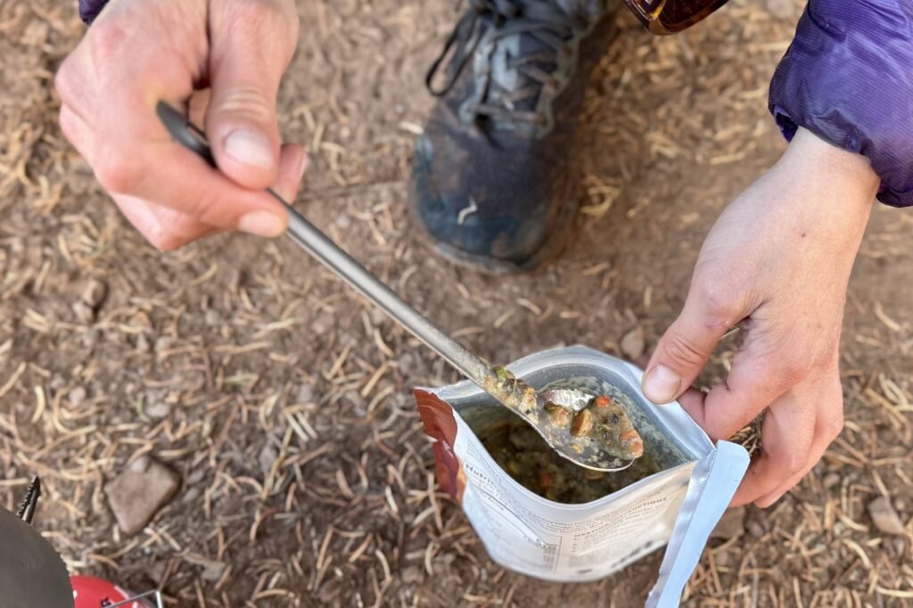 a hiker's hands pull a titanium spoon with food on it from a backpacking meal