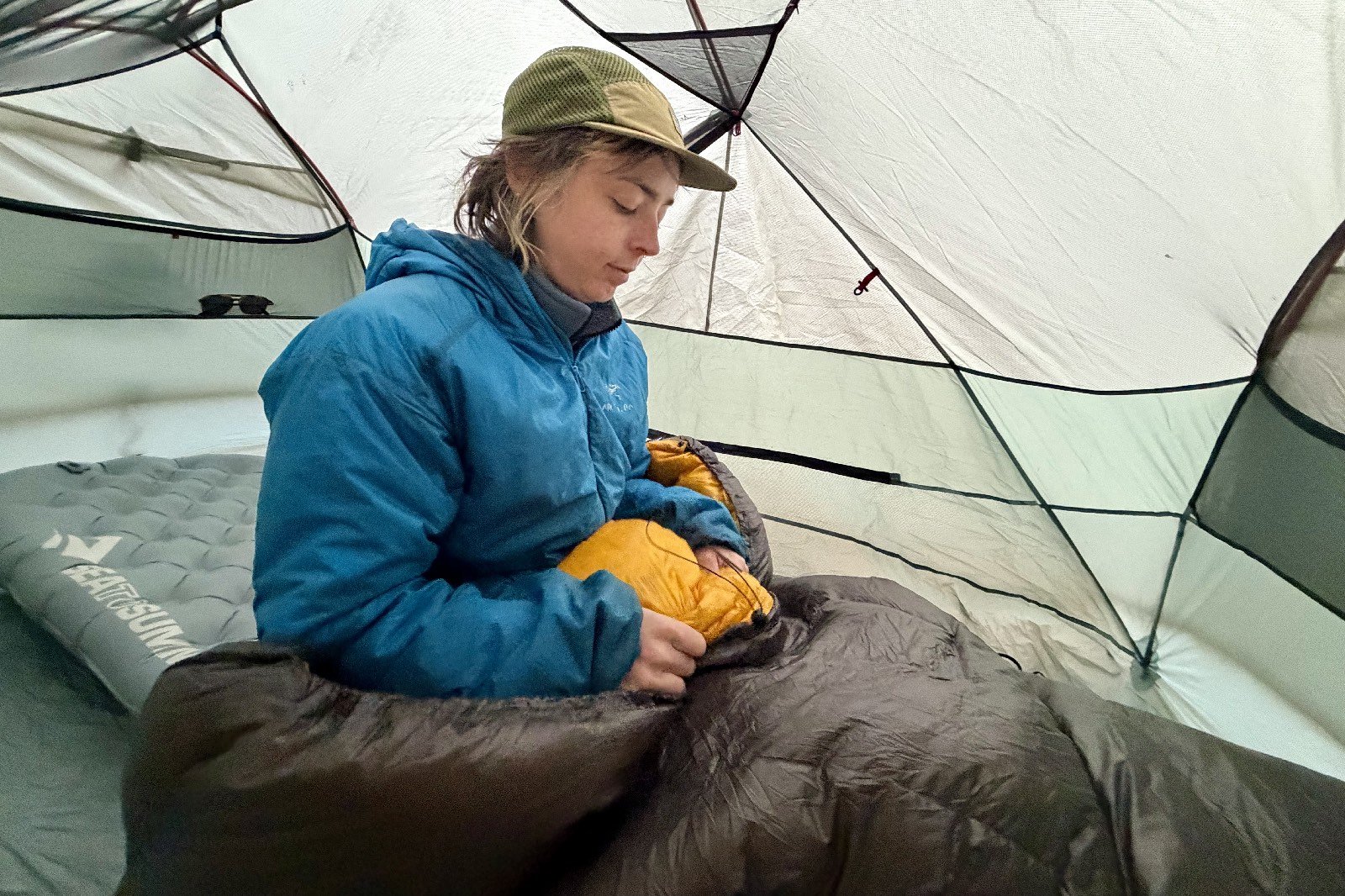 a hiker sits up in a tent with her legs in a grey sleeping quilt