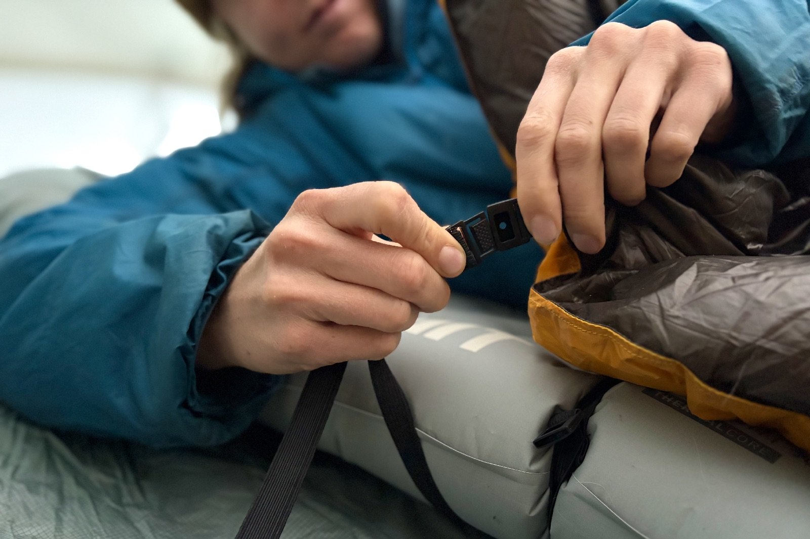 a close up of a hiker buckling a pad strap on a backpacking quilt