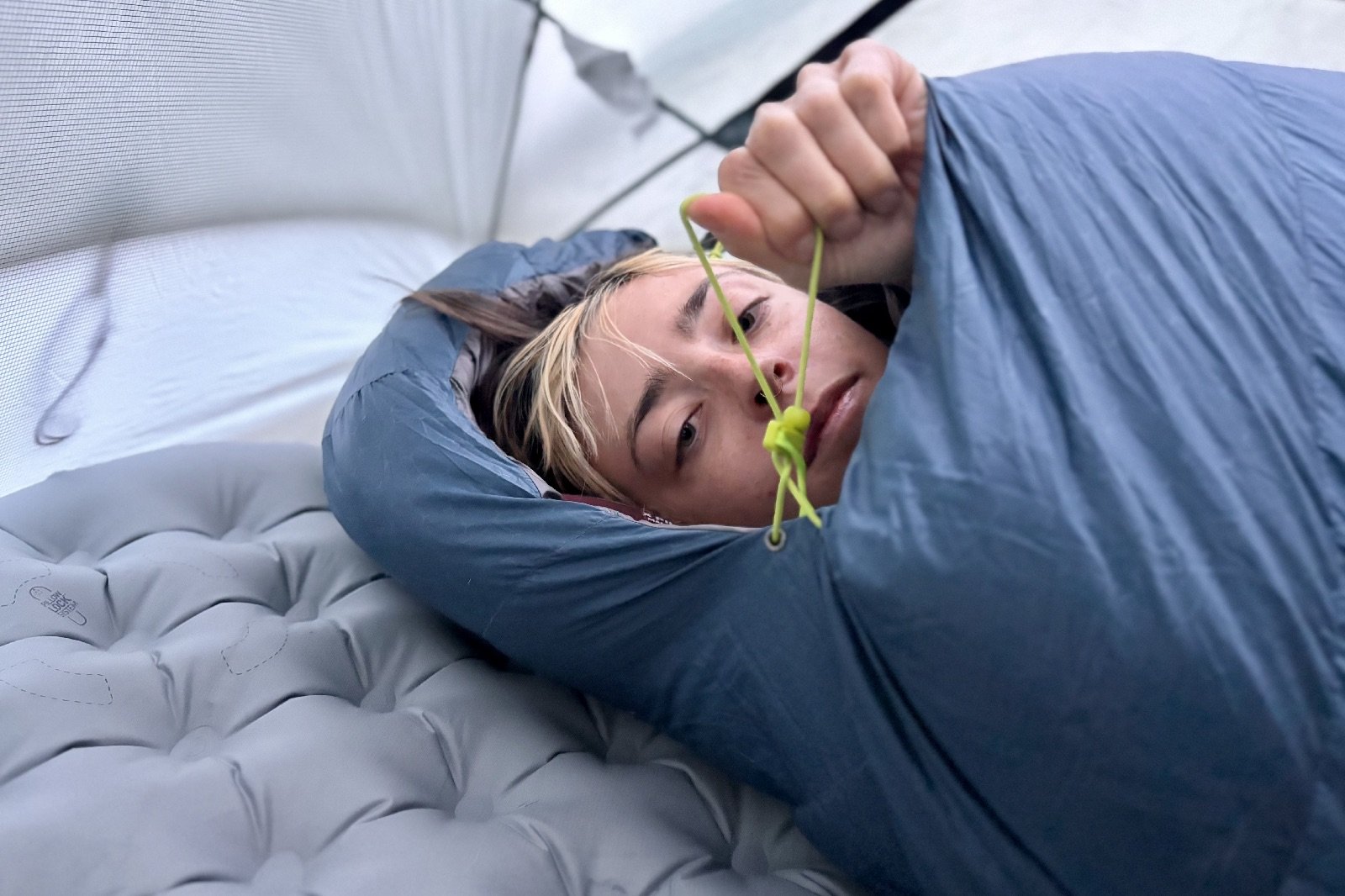 a close up of a hiker in a mummy sleeping bag pulling on the hood drawstring