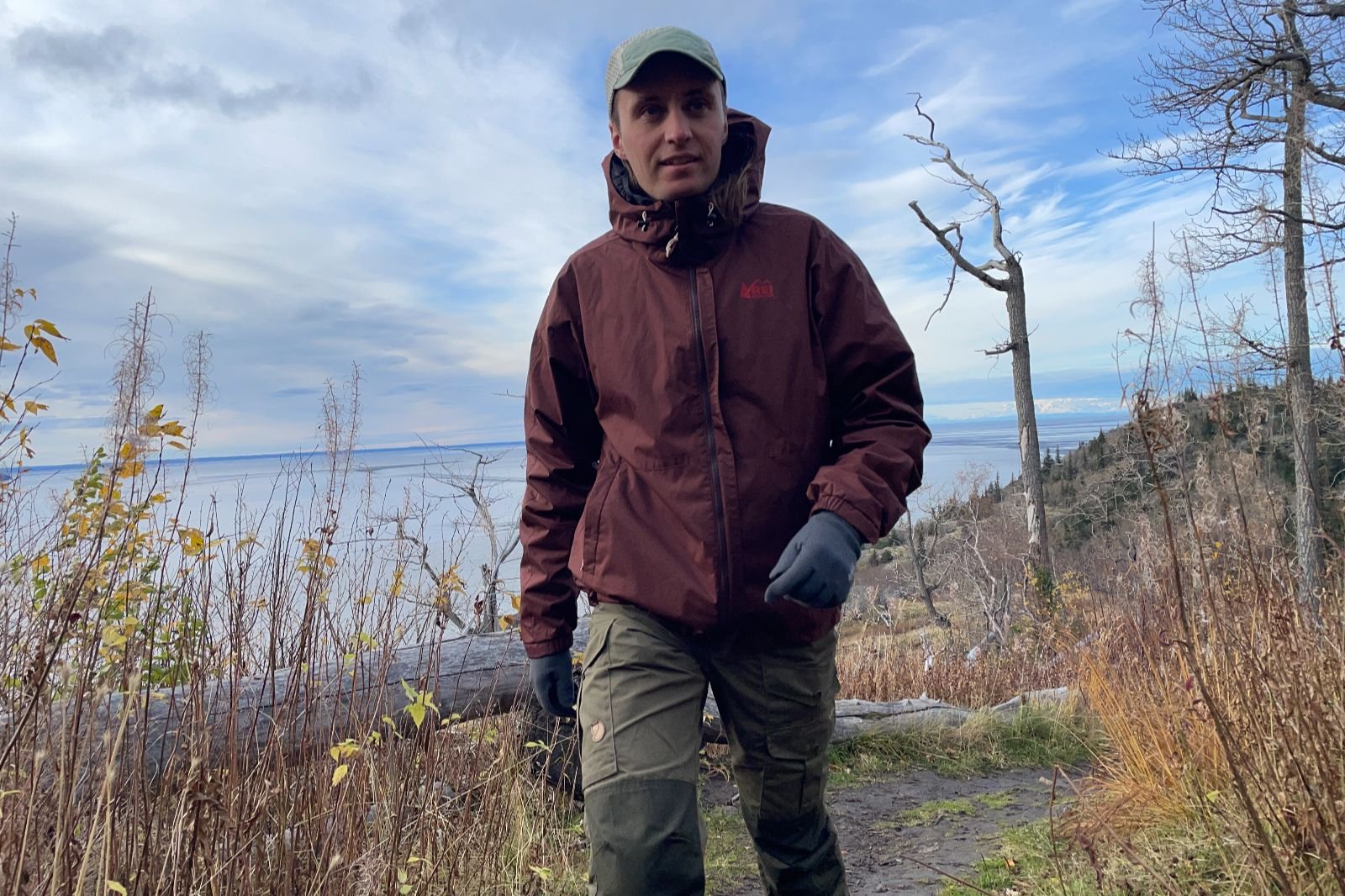 A man hikes uphill wearing a maroon jacket.