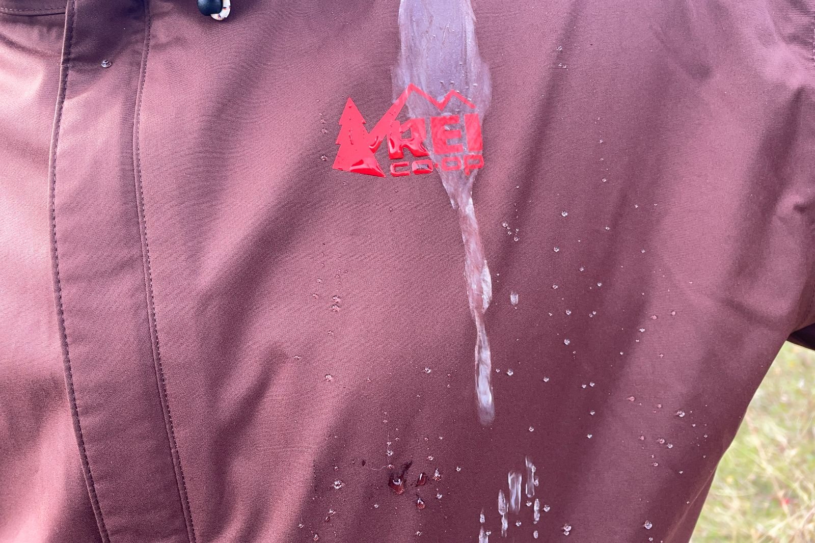 A closeup of water being spilled on a maroon jacket over the logo.