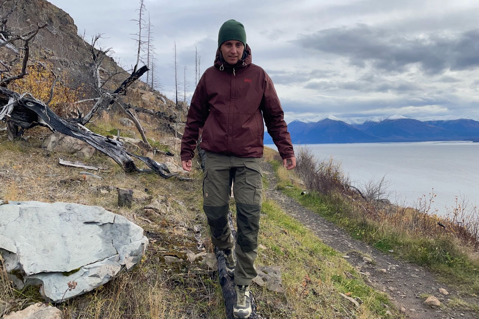A man walks down a log wearing a maroon rain jacket.