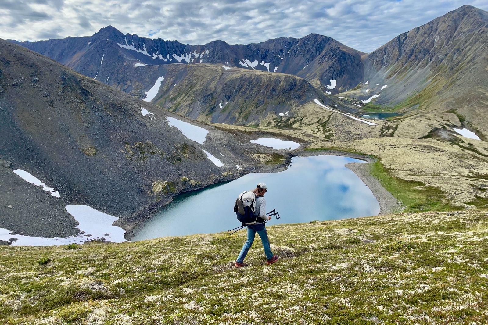 A man descends down an alpine trail to a valley with lakes.
