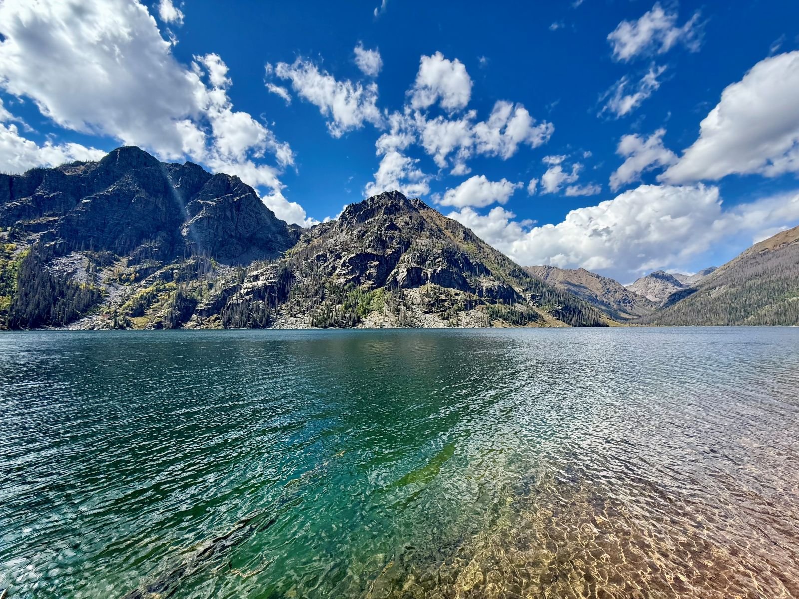 Blue-green water ripples on the surface of an alpine lake framed by rocky mountains in the background