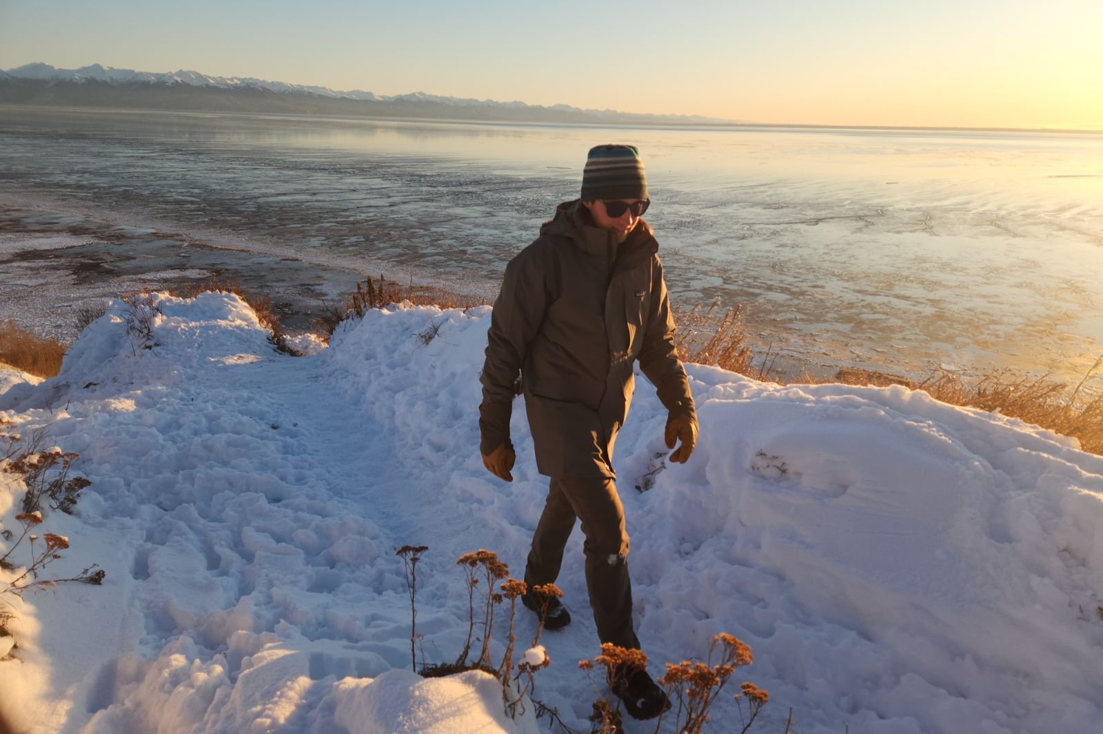 A man hikes up a snowy hill above the ocean.