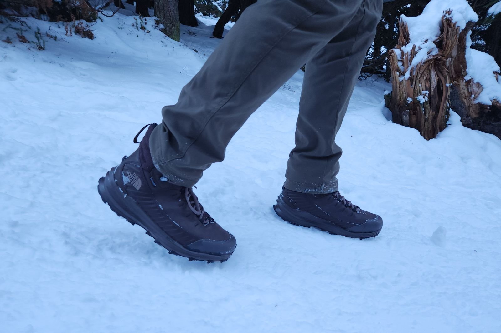 A pair of boots walks downhill on snow.