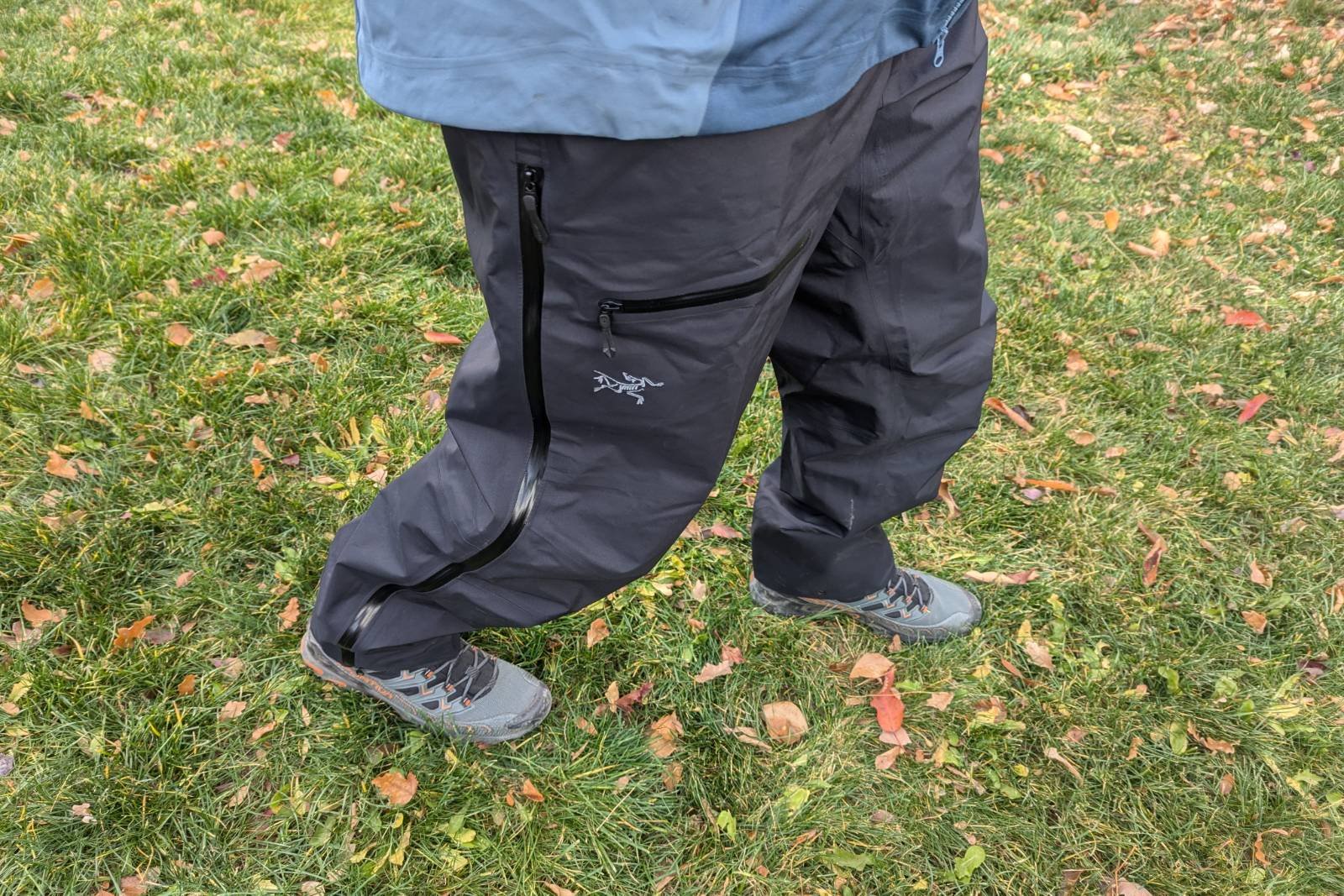 Demonstrating all of the Arc'teryx Beta Pants features from the side standing in grass.