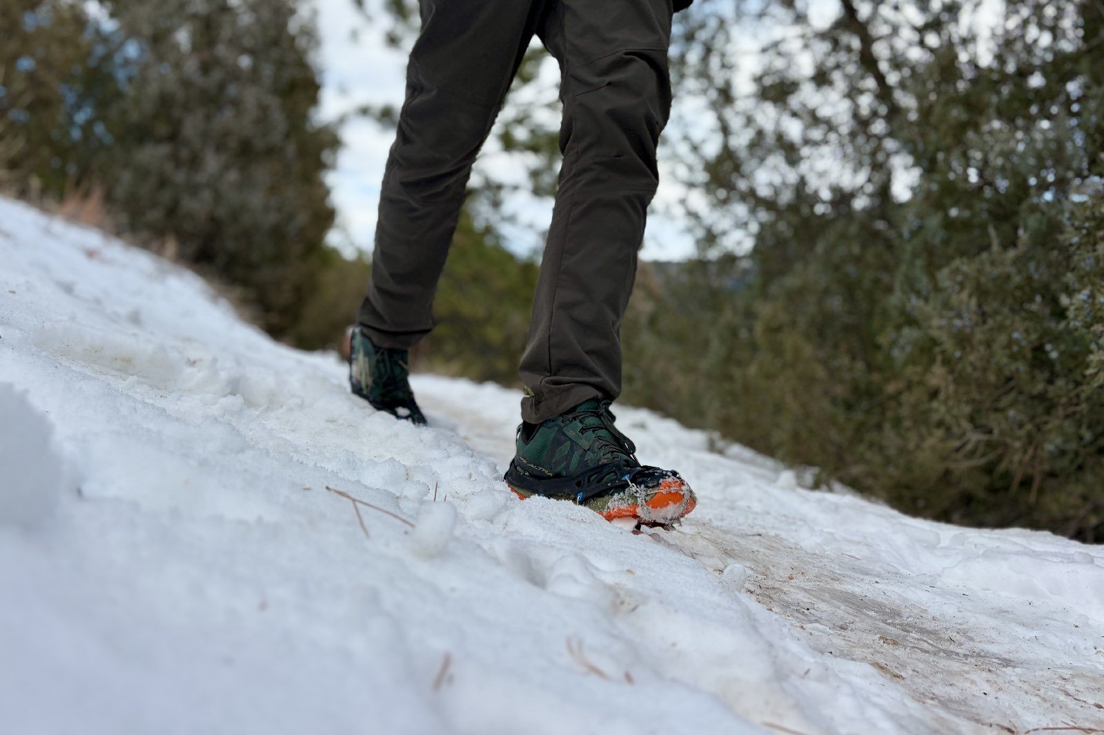 a waist down view of a hiker walking through the snow with a pair of ice cleats