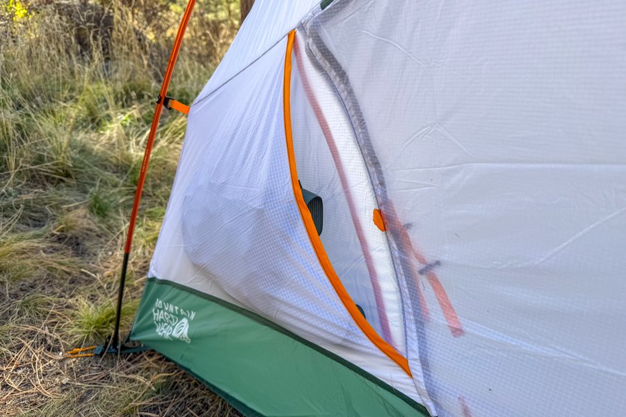 Close-up of the tent’s inner mesh door partially unzipped, showing orange trim, a reinforced zipper path, and the tent body’s green lower panel.