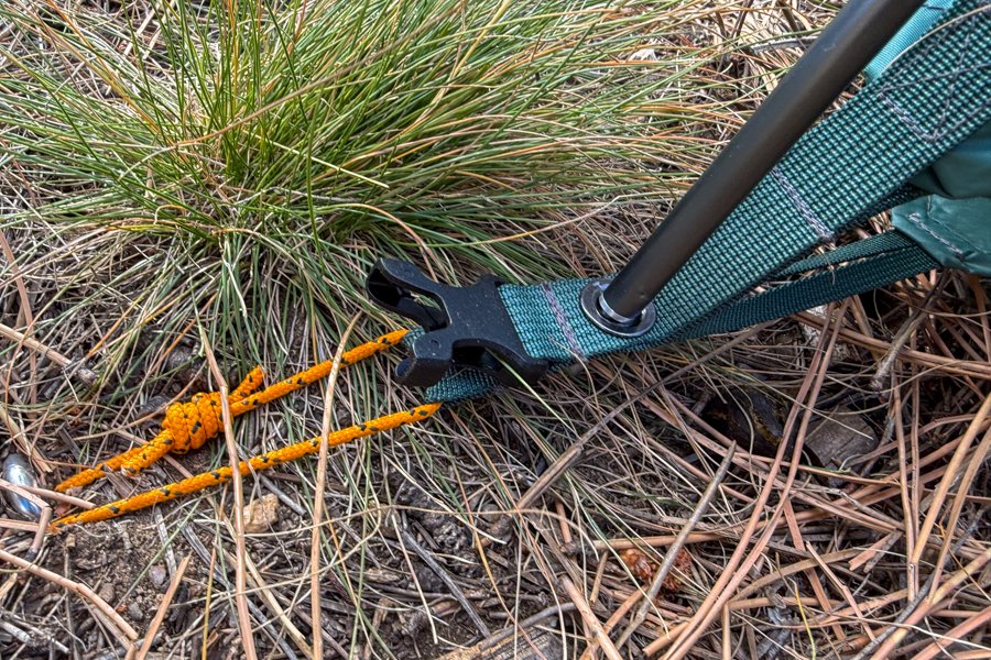 Close-up of the tent’s pole-end interface, showing a pole inserted into a reinforced grommet with guyline tensioned nearby on dry forest ground.